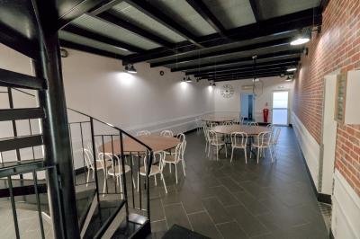 Salle avec des tables rondes et des chaises blanches, éclairée par des lampes suspendues, avec un escalier en colimaçon au…