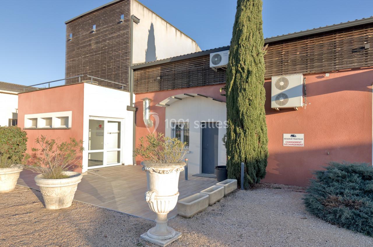 Façade d'un bâtiment moderne avec murs colorés, climatisations extérieures et végétation en pots devant l'entrée.