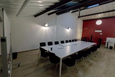 Salle avec des tables rondes, des chaises blanches, un mur en briques et un escalier en colimaçon métallique.