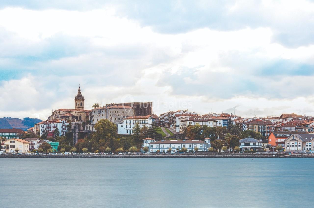 Vue d'une ville côtière avec des bâtiments historiques, une église et des maisons colorées au bord de l'eau.