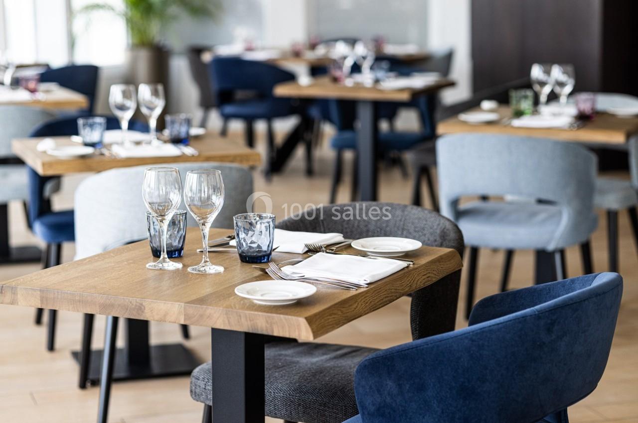 Salle de restaurant moderne avec tables en bois dressées, chaises rembourrées et lumière naturelle.