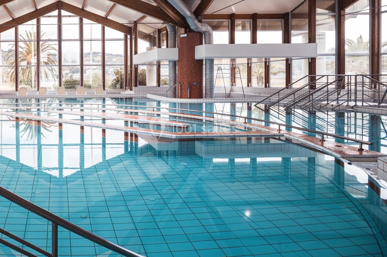Piscine intérieure avec eau claire, rampes d'accès et grandes baies vitrées laissant entrer la lumière naturelle.