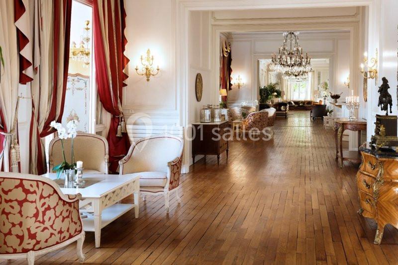 Salon élégant avec parquet en bois, mobilier classique, lustres en cristal et rideaux rouges dans un intérieur lumineux.