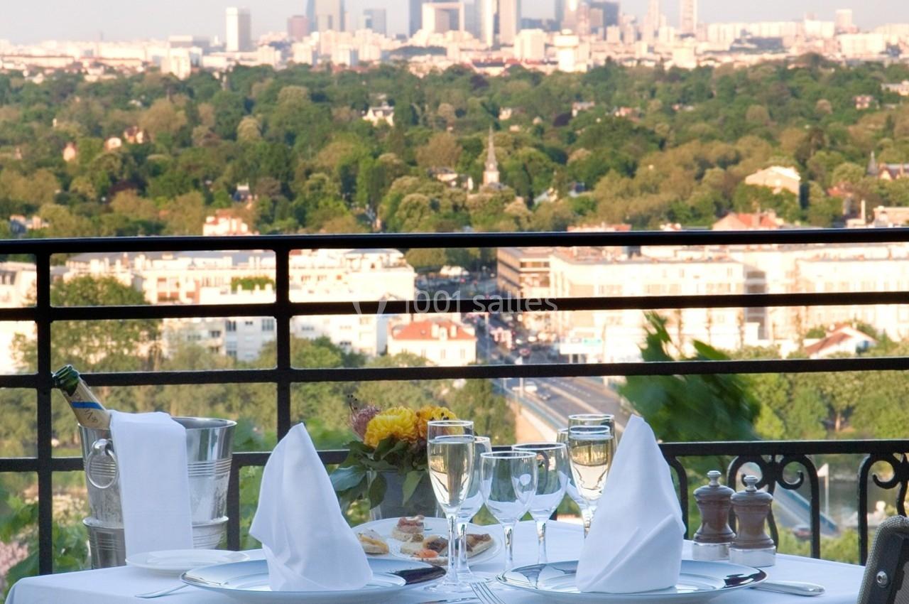 Table dressée avec élégance sur une terrasse, offrant une vue panoramique sur une ville entourée de verdure.