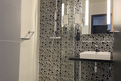 Salle de bain moderne avec douche à l'italienne, carrelage à motifs noirs et blancs, lavabo et miroir éclairé.