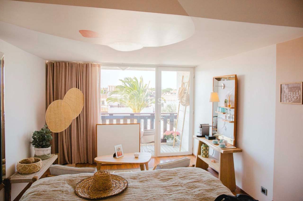 Chambre lumineuse avec balcon, décorée de tons neutres, meubles en bois, et vue sur des palmiers à l'extérieur.