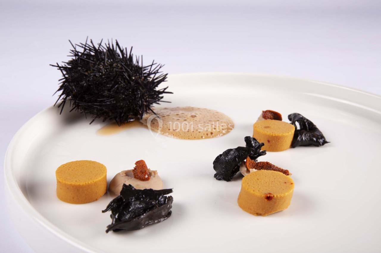 Assiette gastronomique avec oursin, mousse légère, rondelles de préparation orange et garnitures noires.