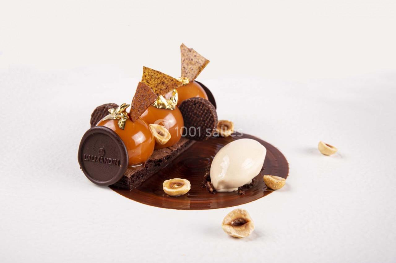 Dessert raffiné composé de sphères caramel, chocolat, noisettes et glace, présenté sur une assiette élégante.