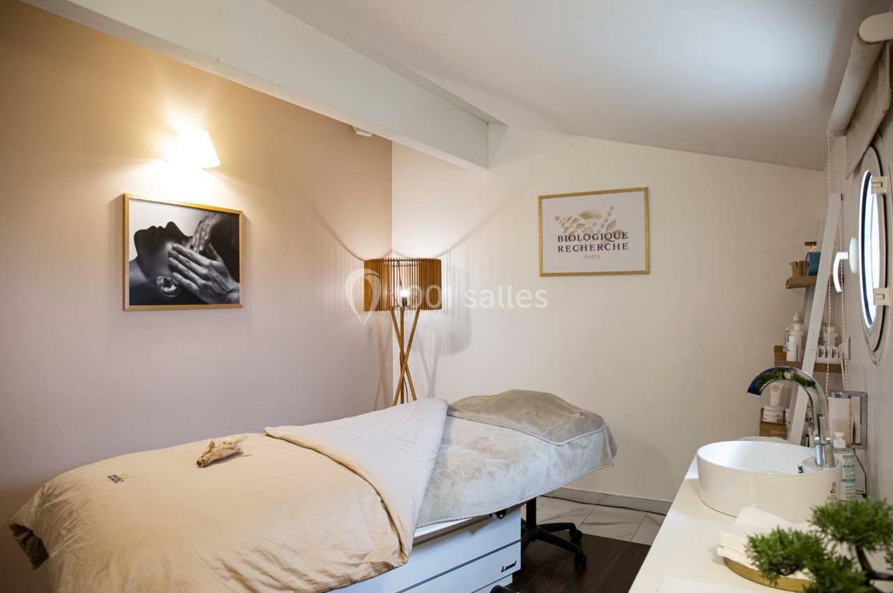 Salle de soin lumineuse avec table de massage, décoration minimaliste et produits de beauté sur une étagère.