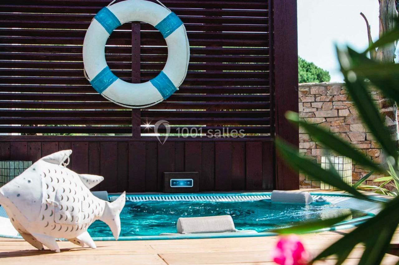 Piscine extérieure avec bouée accrochée à une cloison en bois, décoration en forme de poisson au premier plan.