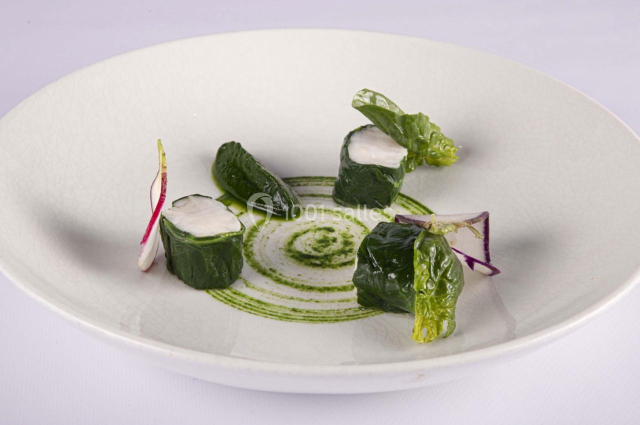 Assiette contenant des rouleaux de légumes verts garnis, accompagnés de feuilles, radis et sauce verte décorative.