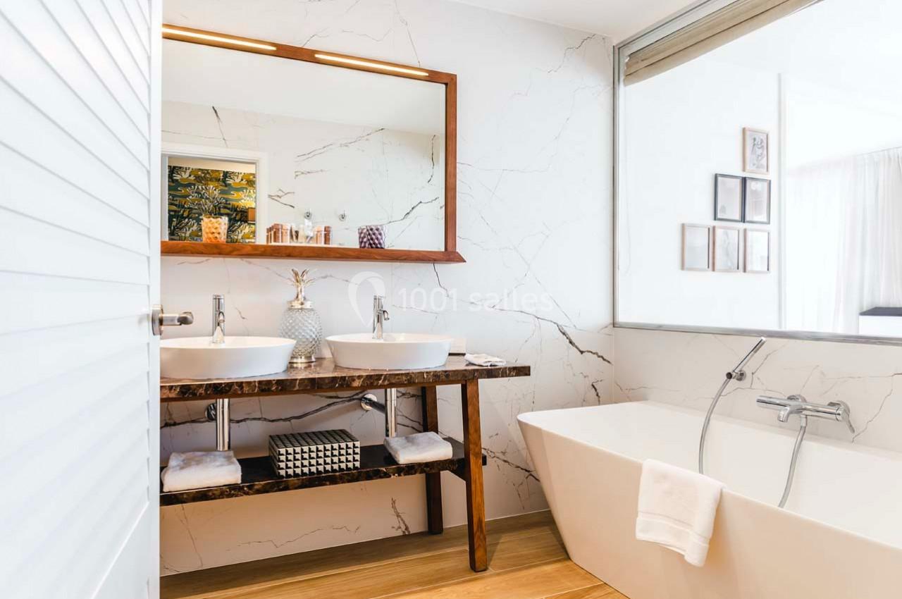 Salle de bain moderne avec deux vasques, un miroir encadré en bois, une baignoire et un décor lumineux.