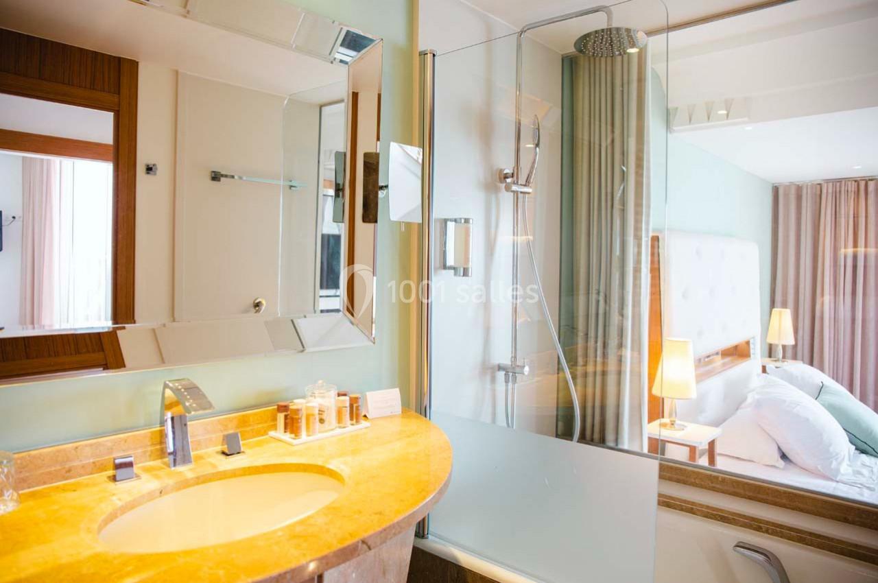 Salle de bain moderne avec lavabo en marbre, douche vitrée et vue partielle sur une chambre lumineuse.