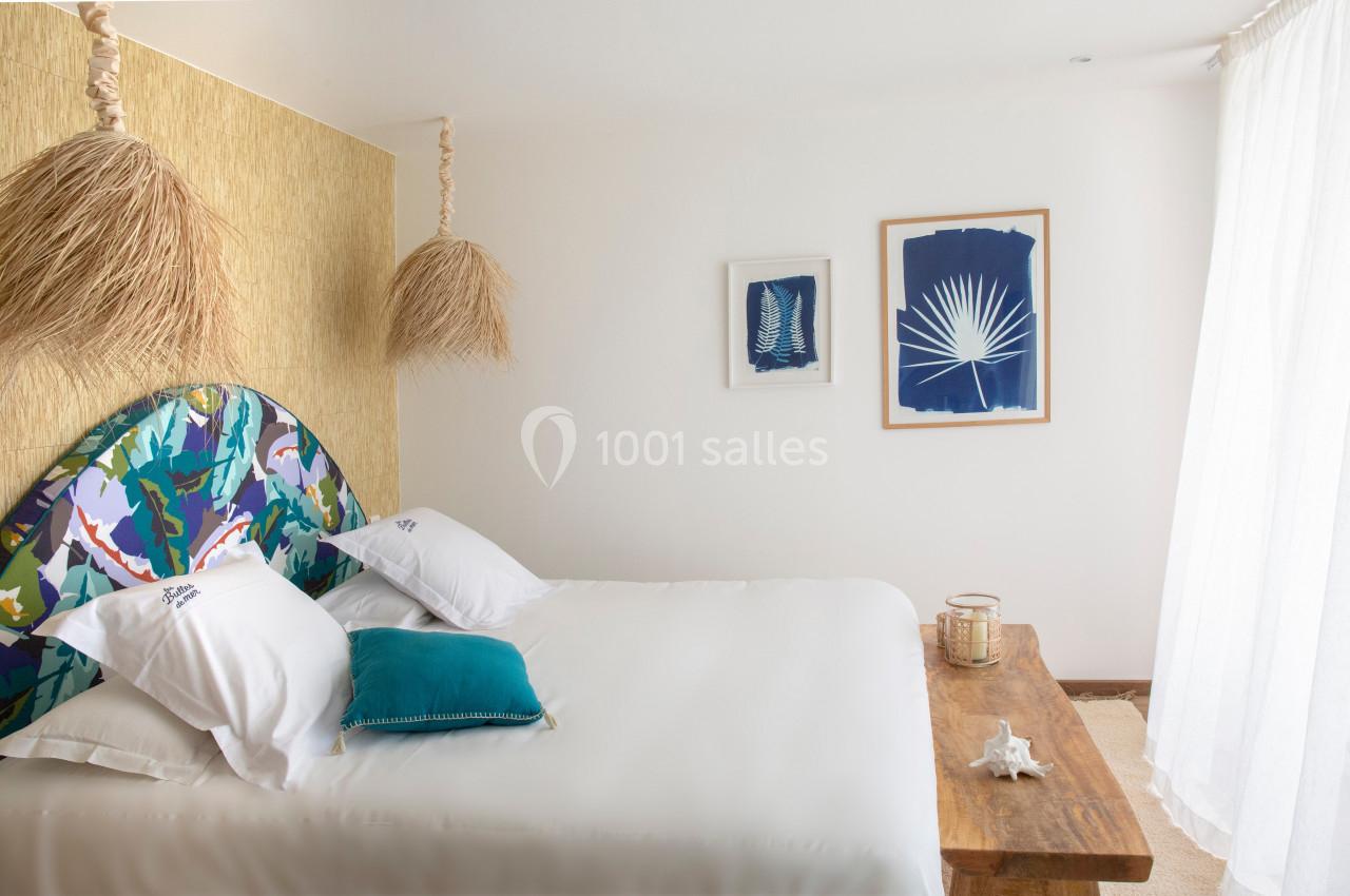 Chambre lumineuse avec lit double, tête de lit colorée, décorations murales bleues et table en bois rustique.