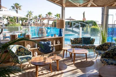 Terrasse ensoleillée avec tables et chaises bleues, décorée de plantes et d'un panneau indiquant ’La plage’.