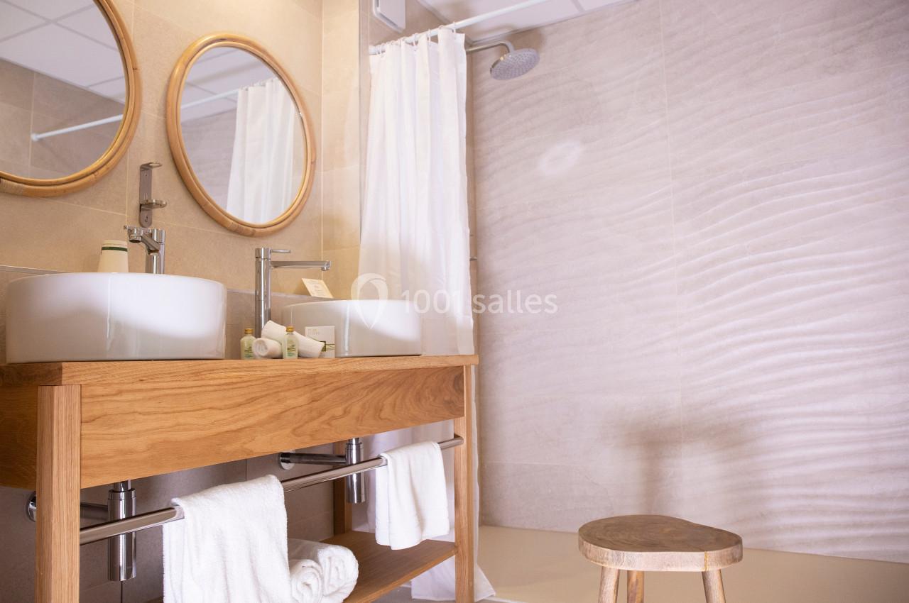 Salle de bain moderne avec double vasque en bois, miroirs ronds, douche à l'italienne et tabouret en bois.