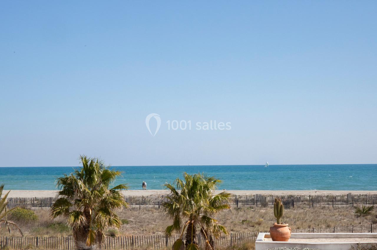 Vue sur une plage bordée de palmiers, avec une mer calme et un ciel dégagé à l'horizon.