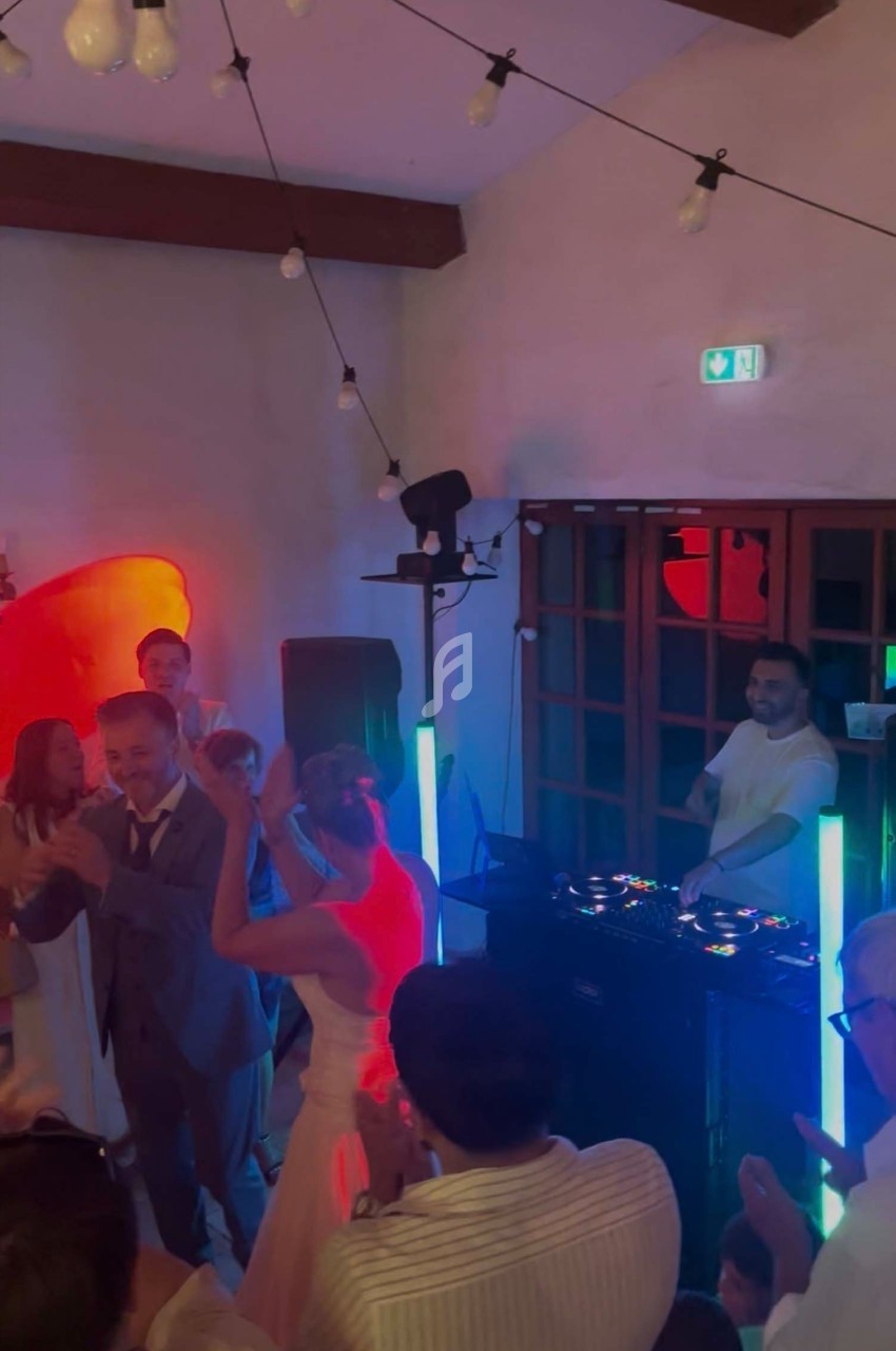 Des invités dansent autour d'un DJ lors d'une fête dans une salle éclairée par des lumières colorées.