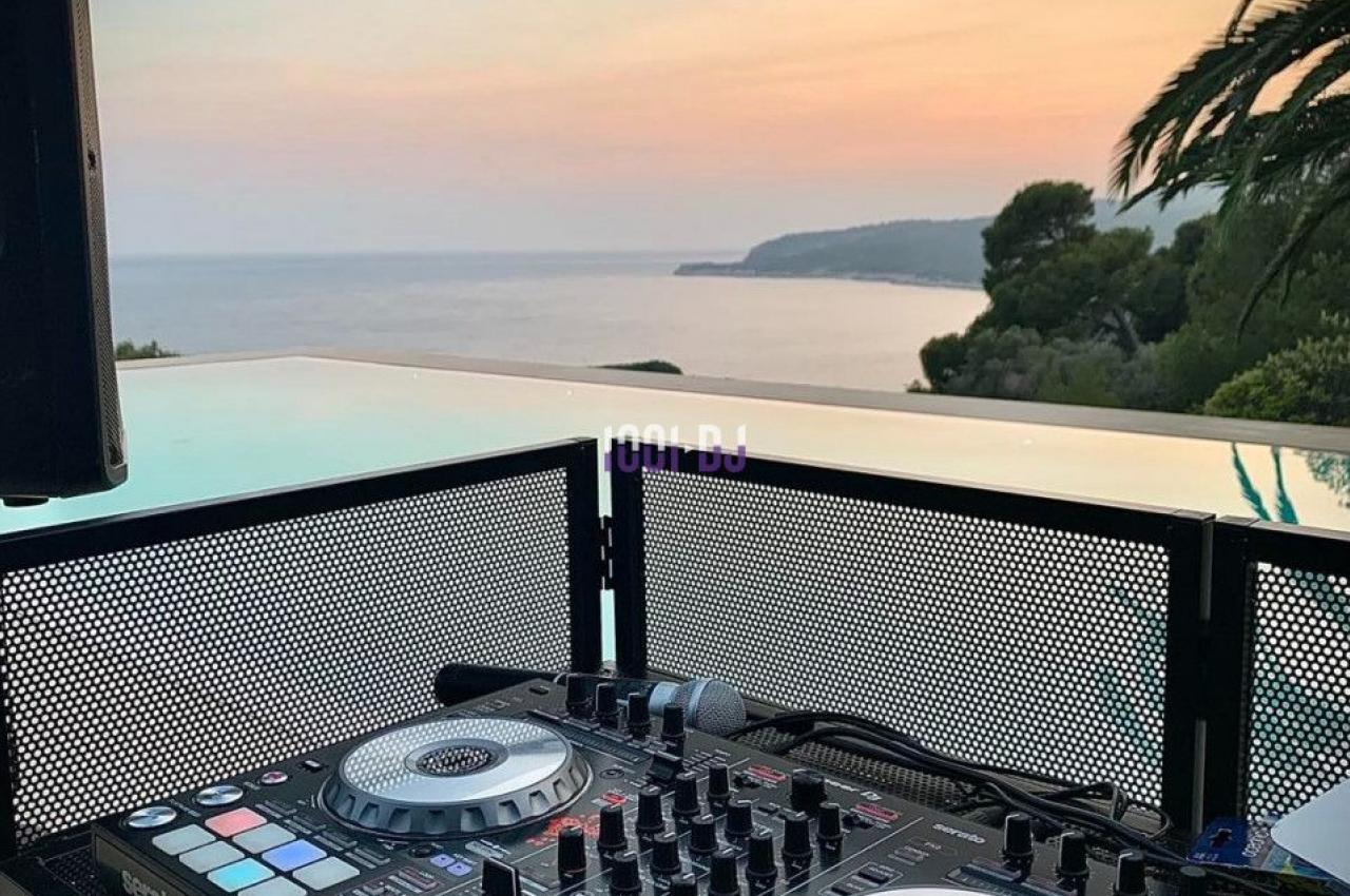 Table de mixage DJ installée en extérieur avec vue sur la mer au coucher du soleil.