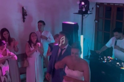 Un couple danse entouré d'invités dans une salle éclairée par des lumières colorées, avec un DJ en arrière-plan.