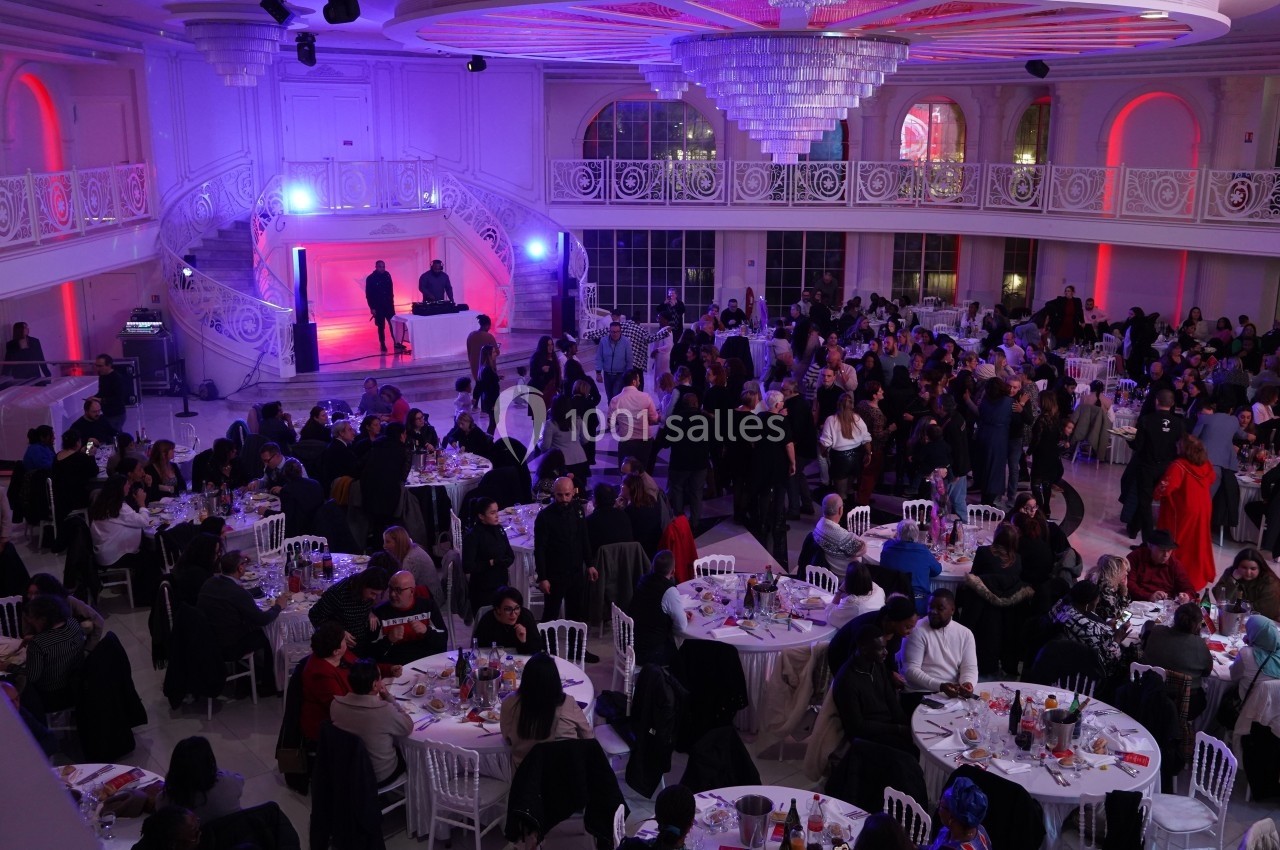 Salle de réception éclairée en violet et rouge, remplie d'invités assis à des tables rondes lors d'un événement.