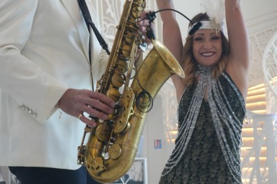 Un musicien jouant du saxophone accompagné d'une femme souriante dansant dans un décor élégant.