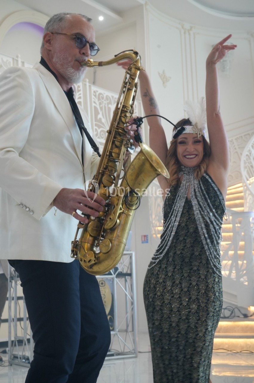 Un musicien jouant du saxophone accompagné d'une femme souriante dansant dans un décor élégant.