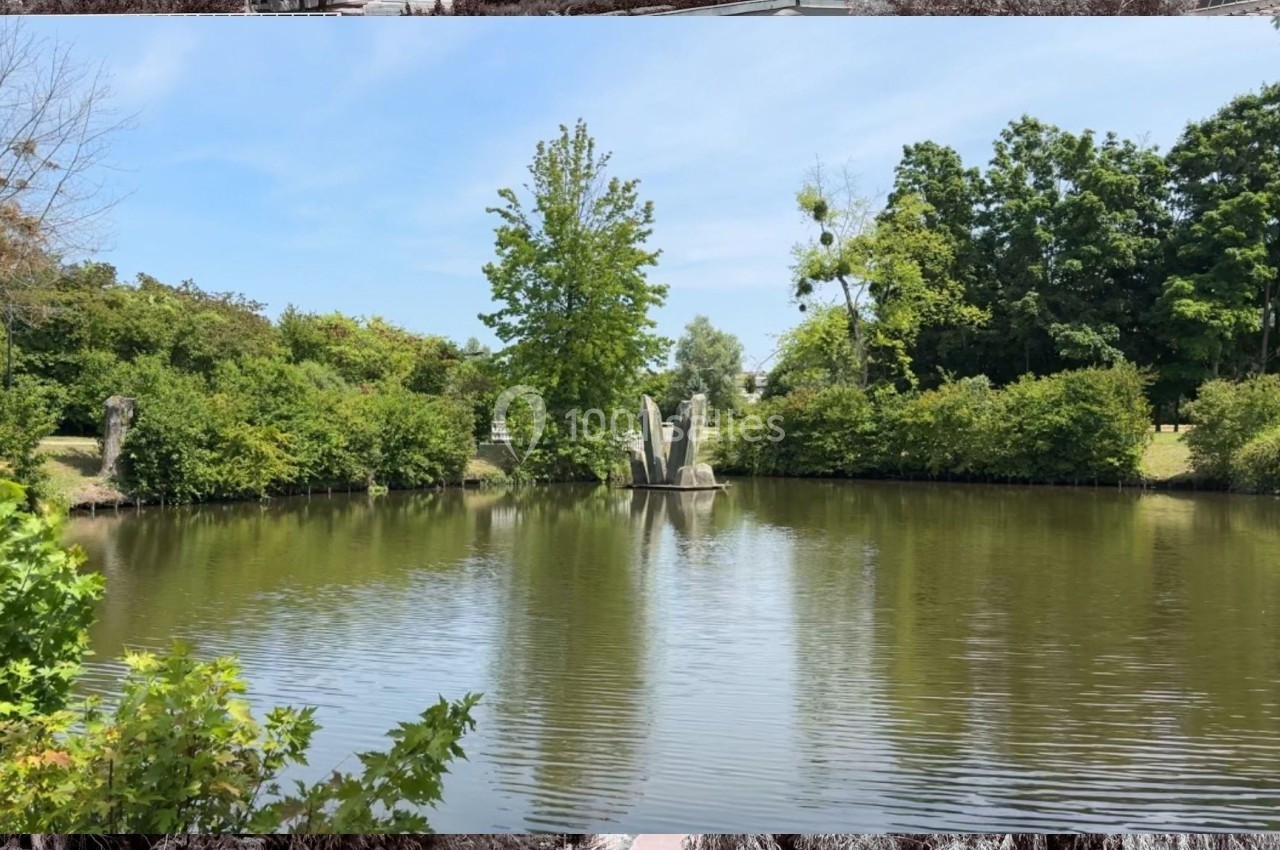 Étang entouré de verdure avec une sculpture centrale composée de formes verticales en pierre.