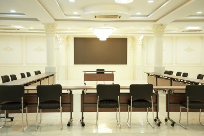 Salle de conférence lumineuse avec tables disposées en U, chaises noires et un tableau noir au fond.
