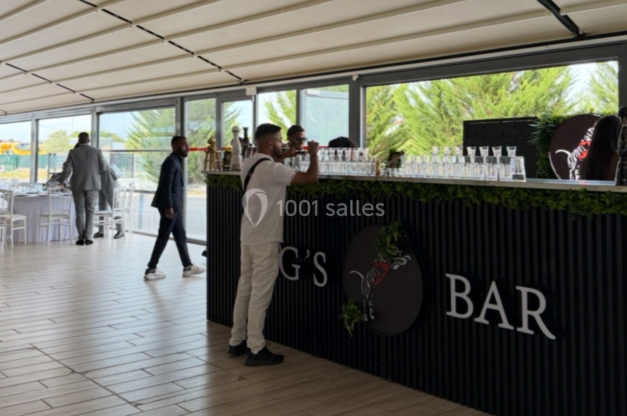 Un homme commande au bar d'un espace lumineux avec des tables dressées en arrière-plan.