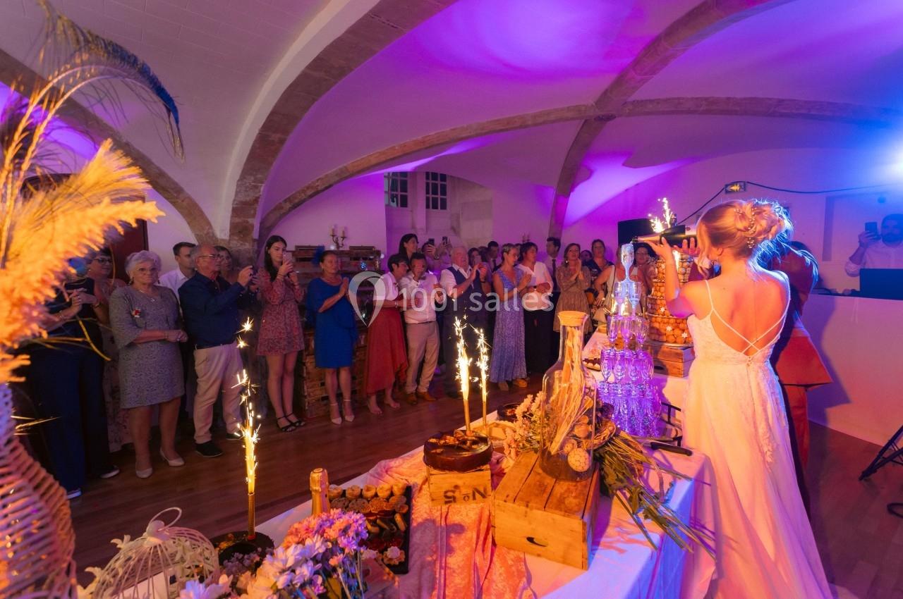 Une mariée de dos face à des invités applaudissant dans une salle décorée, avec des étincelles sur une table festive.