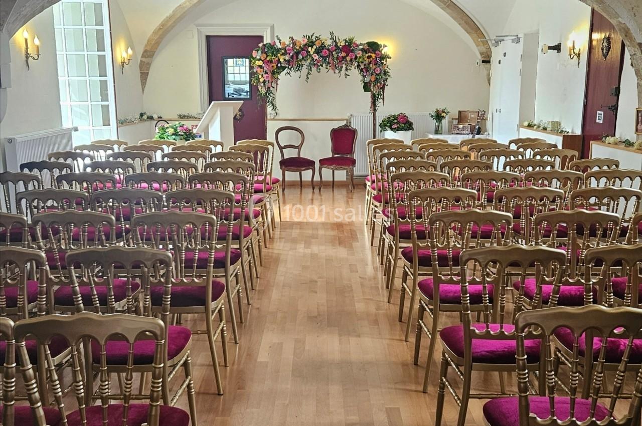 Salle de cérémonie avec des chaises dorées à assise rouge, un autel fleuri et une arche décorative en arrière-plan.