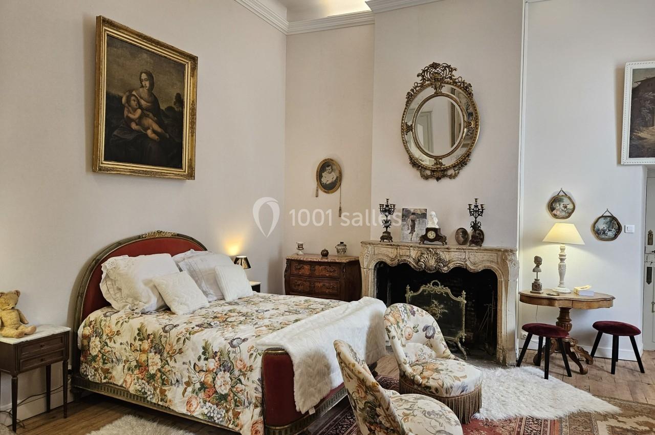 Chambre élégante avec lit à motifs floraux, cheminée ornée, miroir doré et décorations murales classiques.