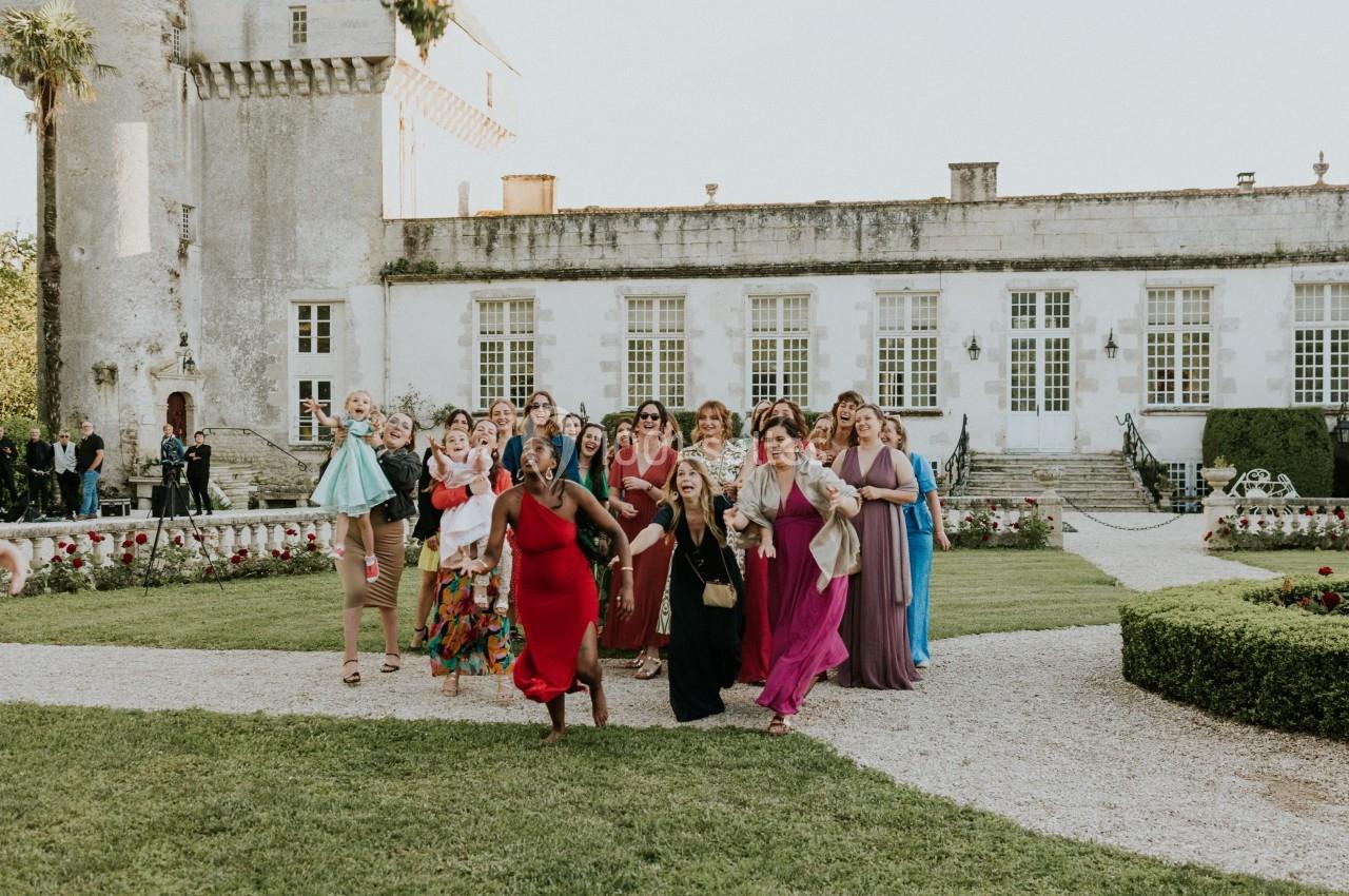 Un groupe de femmes élégamment vêtues marche joyeusement dans un jardin devant un bâtiment historique.