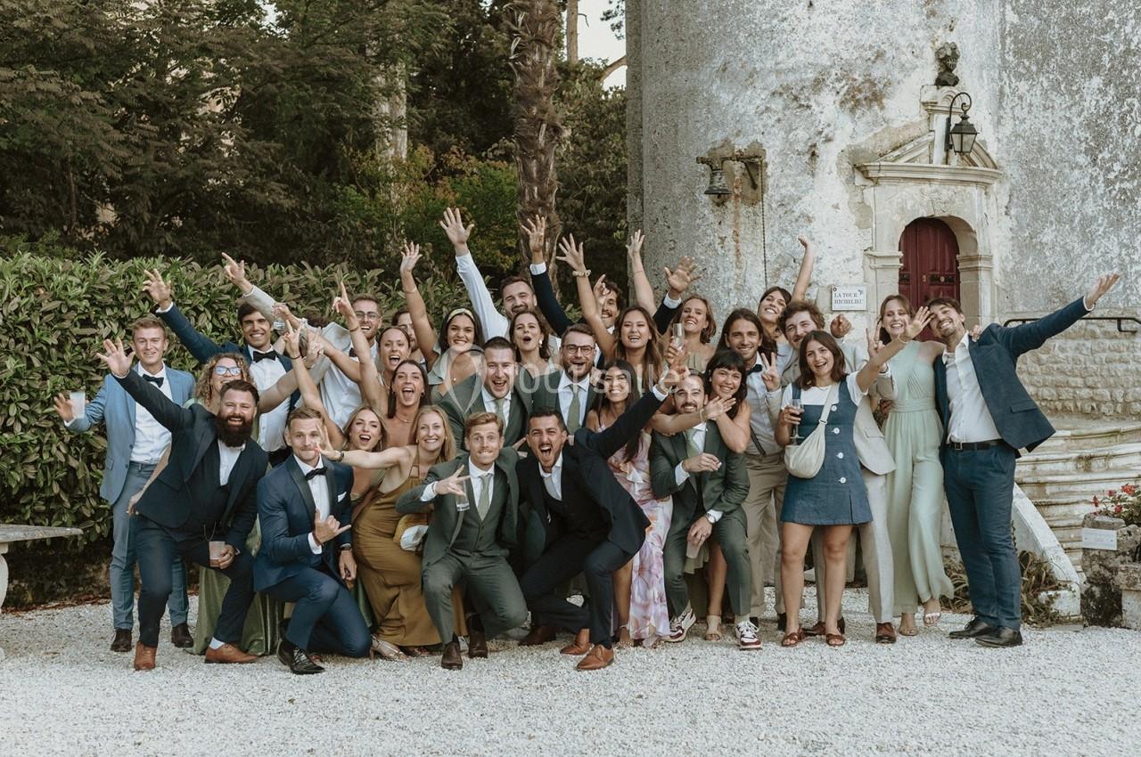Un grand groupe de personnes souriantes posant devant un bâtiment ancien, bras levés dans une ambiance festive.