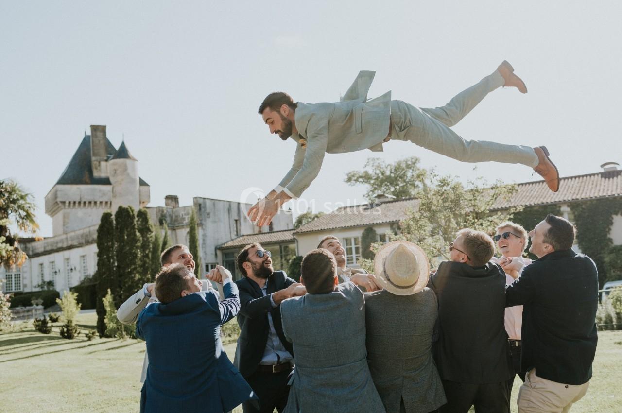 Un groupe d'hommes en costume lance un homme en l'air dans un jardin devant un bâtiment ancien.