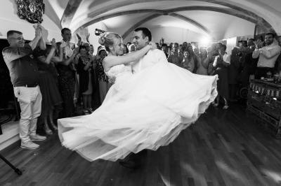 Un couple de mariés s'embrasse devant des invités applaudissant dans une salle de réception lumineuse.