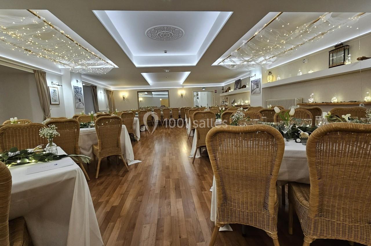 Salle de réception décorée avec des guirlandes lumineuses, des tables dressées et des chaises en rotin.
