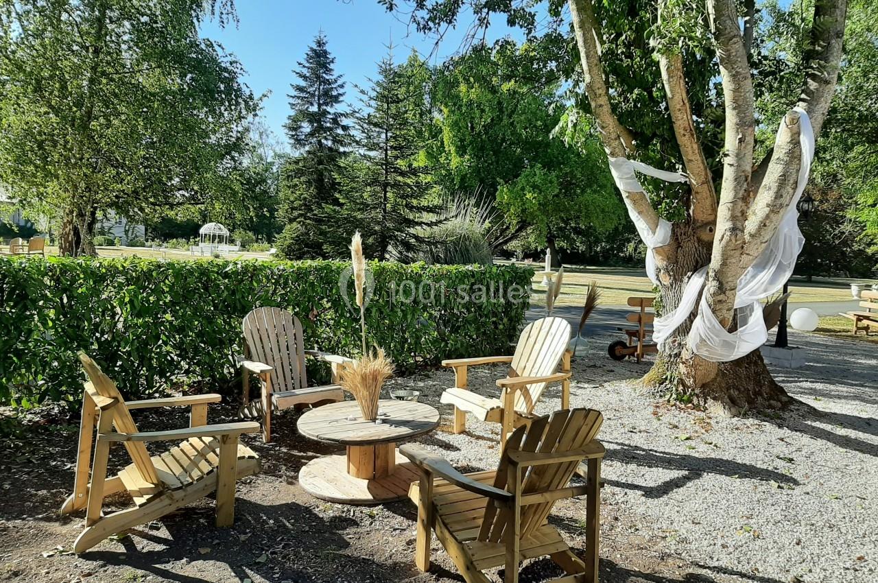 Quatre chaises en bois disposées autour d'une table basse en extérieur, sous des arbres avec des décorations en tissu.