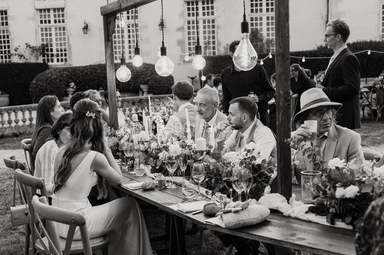 Des invités discutent et dînent à une table décorée de fleurs et de guirlandes lumineuses dans un jardin.