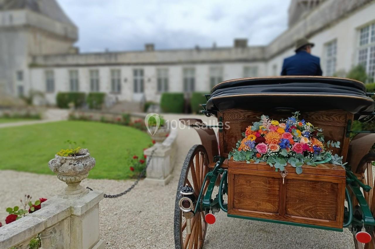 Calèche décorée de fleurs colorées stationnée dans une cour pavée devant un bâtiment ancien.