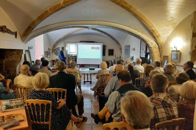 Des personnes en costumes d'époque discutent dans la cour d'un château historique sous un ciel partiellement nuageux.