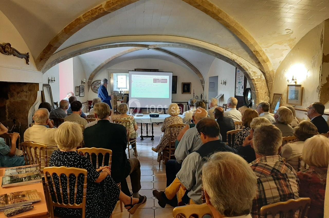 Un groupe de personnes assises dans une salle voûtée, écoutant une présentation projetée sur un écran.