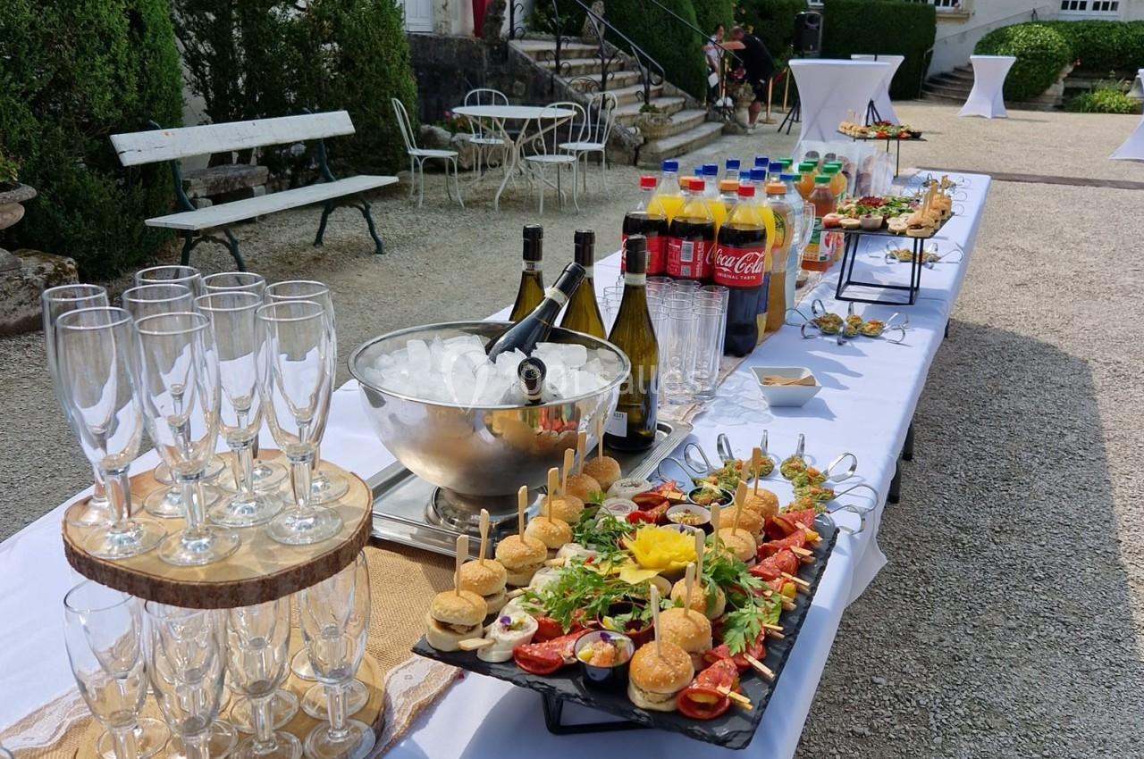 Buffet en extérieur avec verrines, amuse-bouches, boissons et coupes de champagne, disposés sur une table blanche.