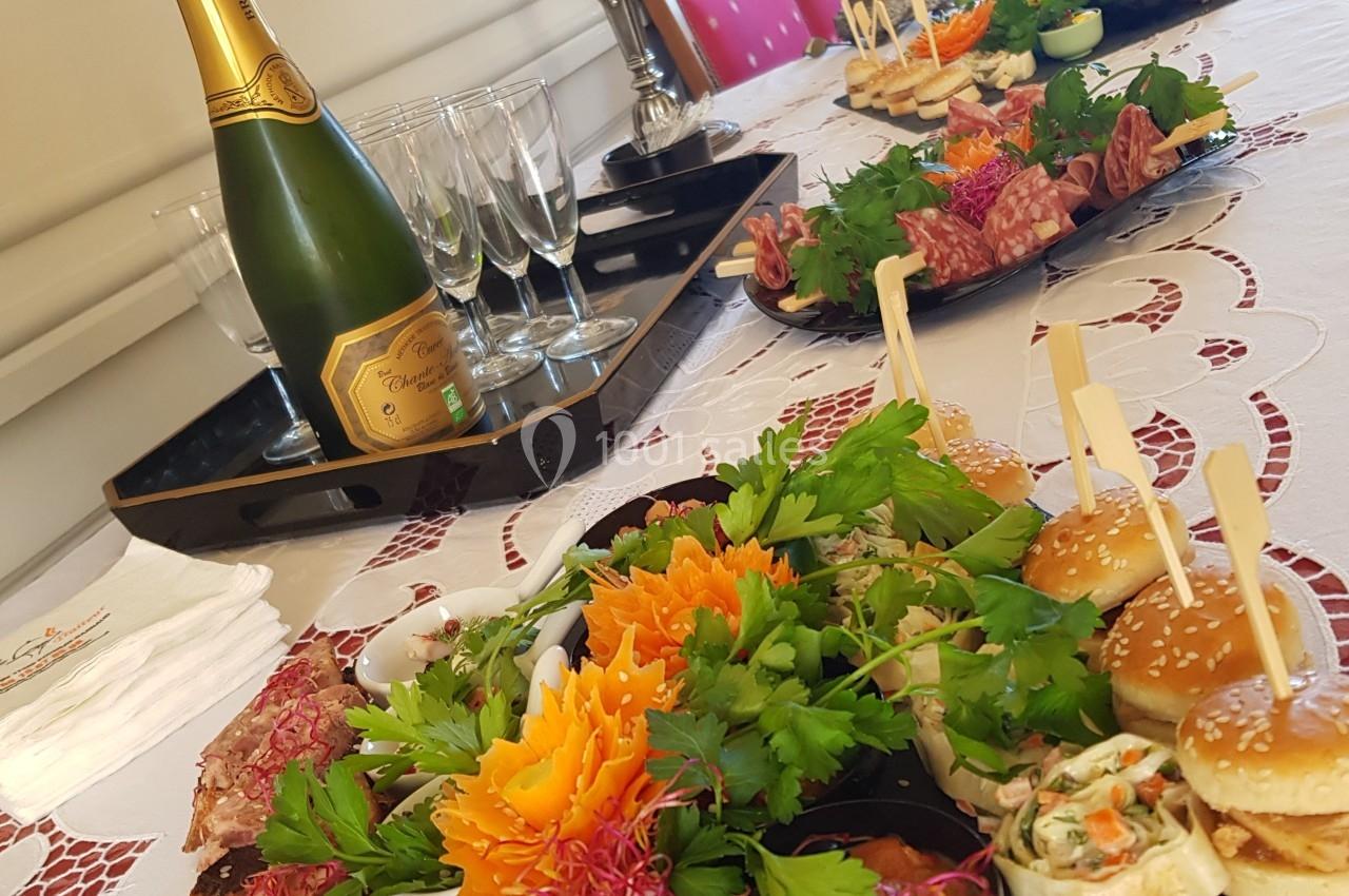 Plateau de mets variés avec charcuteries, légumes, mini-burgers et bouteille de champagne sur une table décorée.