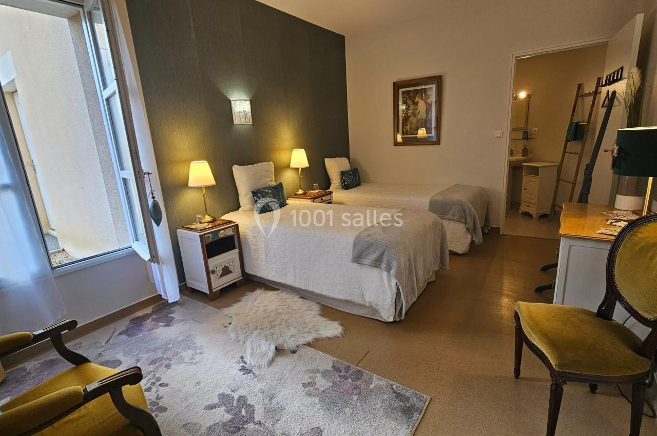 Chambre lumineuse avec deux lits simples, mobilier classique, tapis fleuri et vue sur une fenêtre donnant sur l'extérieur.