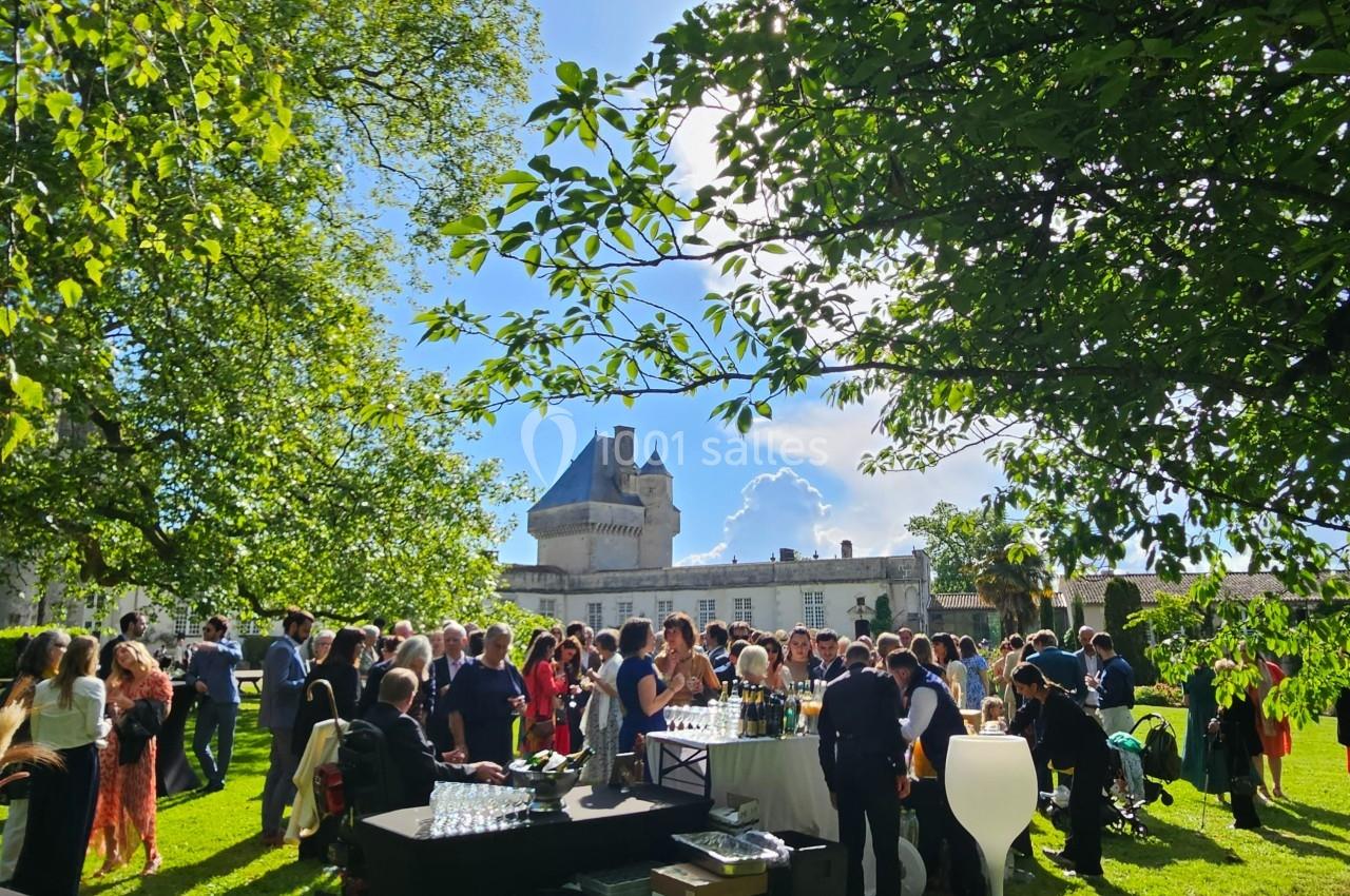 Groupe de personnes rassemblées dans un jardin verdoyant près d'un château sous un ciel ensoleillé.
