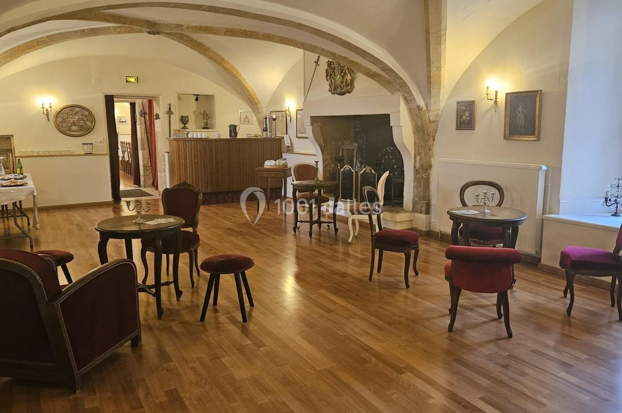 Salle avec parquet, tables et chaises disposées, murs ornés de tableaux et poutres apparentes au plafond.