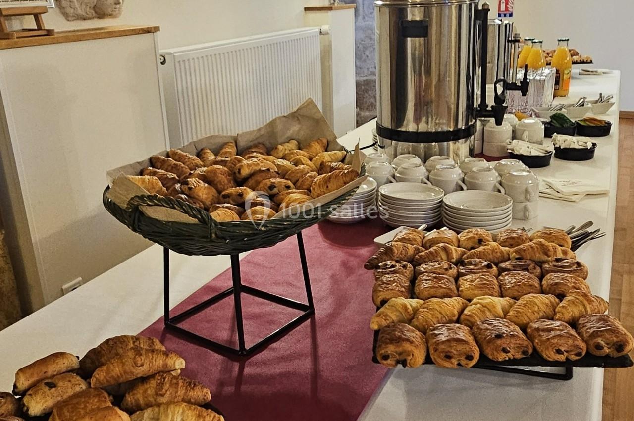 Buffet de petit-déjeuner avec viennoiseries, boissons chaudes, jus de fruits et serviettes sur une table dans une salle…