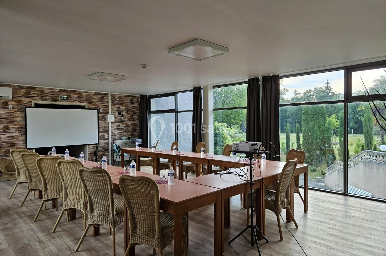 Salle de réunion lumineuse avec grandes baies vitrées, tables en bois, chaises en osier et matériel de présentation.